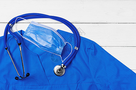 白色木质背景上带听诊器和面罩的医生医用制服实验室卫生流感口罩危害工具预防装置测量科学图片