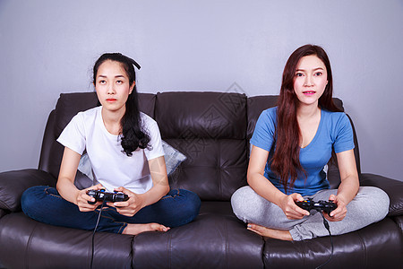两个年轻女子在家沙发上玩电子游戏 使用棍棒控制器女性娱乐乐趣游戏房间快乐姐妹友谊女士长椅图片