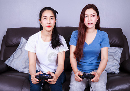 两个年轻女子在家沙发上玩电子游戏 使用棍棒控制器乐趣竞赛幸福安慰朋友们快乐活动姐妹女士友谊图片