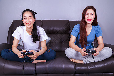 两个年轻女子在家沙发上玩电子游戏 使用棍棒控制器女士长椅友谊技术活动闲暇成人游戏乐趣快乐图片