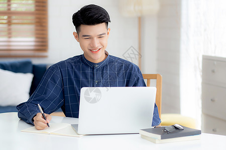 年轻的亚洲商务人士在笔记本上写作 以计划在家里的办公桌上工作和使用笔记本电脑 记下金融 男性学习和学习 商业和沟通概念商务员工营图片
