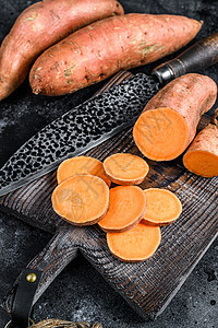 木制切削板上的甜土豆 黑色背景 顶层视图黄色蔬菜番薯红色橙子食物烹饪饮食乡村块茎图片