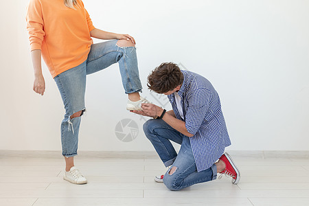 年轻男子正在跪下 并尊崇地将鞋带绑在身上 用白色背景摆着的无名化身份不明妇女身上 主导关系的概念微笑经理学生工作室女孩商务女性工图片