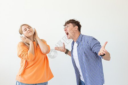 年轻的心烦意乱的男人恳求他的女人听他说 但她戴着耳机听音乐 背景是白色的 误解和不愿意进行对话男性工作女性快乐衣服经理牛仔裤人士图片