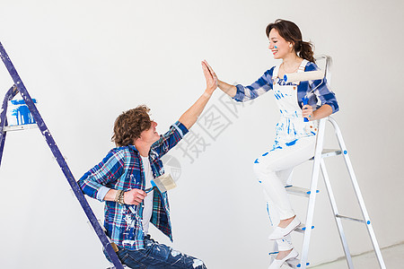 男人坐在梯子上团队合作 翻新和重新装修的概念  坐在梯子上涂着油漆的年轻男女配件家庭胶水改造女孩衬衫夫妻艺术女士男性背景