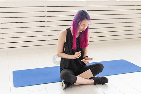 穿着紫色头发的漂亮年轻混血女孩坐在健身房运动垫子上时 用智能手机上的应用程序计算着烧焦热量 瑜伽和健身概念锻炼活动护理训练成人有图片
