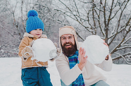 冬天 父子俩在户外玩耍 享受大自然的冬天 爸爸和孩子在雪花园的冬天画像 父亲和儿子在冬天的背景下做雪球图片