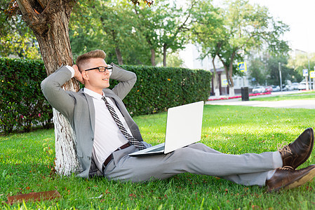 手持笔记本电脑的公园商务人士男性教育花园草地男生人士思考树木快乐商务图片