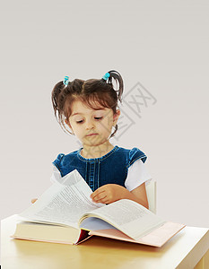 小女孩在桌子上看一本书教育童年学习孩子们女学生灰色学生乐趣学校快乐图片