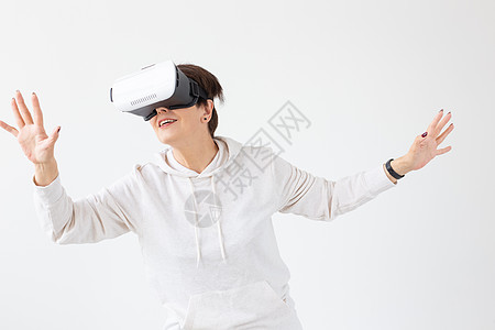 穿着轻毛衣的不明身份中年妇女玩3D游戏 在白色背景上戴虚拟现实眼镜 针对老年人的高科技概念 高科技快乐成人微笑黑发冒充女士女性喜图片