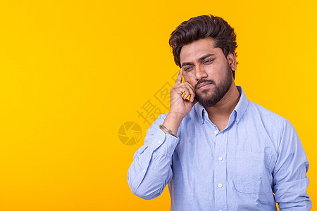 时髦忧伤沉思的印度年轻人 留着胡子 穿着蓝色衬衫 背景是黄色 广告空间 思维的概念图片