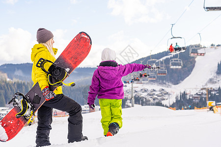 母亲和女儿带着雪板在雪中玩耍旅行女士女性女孩幸福高山缆车行动童年天空图片