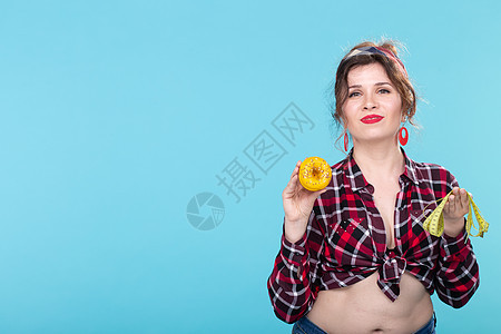 饮食 减肥和垃圾食品 — 年轻女性在带复制空间的蓝色背景中选择甜甜圈和测量类型图片