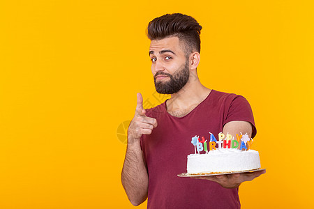 留着胡子的年轻男性嬉皮士拿着一个蛋糕 上面写着生日快乐 祝贺周年纪念日和节日 促销和折扣的概念成人身体姿势人士冒充胡须乐趣头发男图片