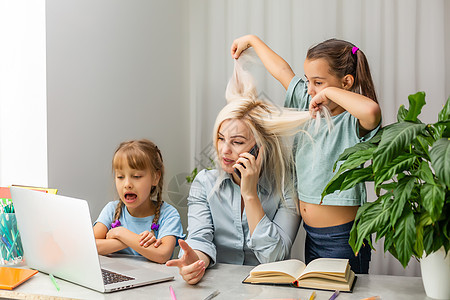 在笔记本电脑上工作的母亲疲劳母亲和两个女儿玩游戏商务办公室人士情感童年妈妈女士孩子们技术孩子图片