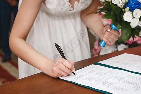 婚礼上一位年轻女孩新娘的手在登记处的文件中签署了同意结婚的签名图片