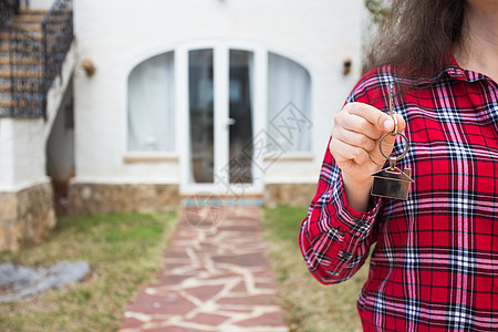 房地产和财产概念 — 在新家前 妇女拿着房子钥匙挂在房子形状的钥匙链上的特写图片
