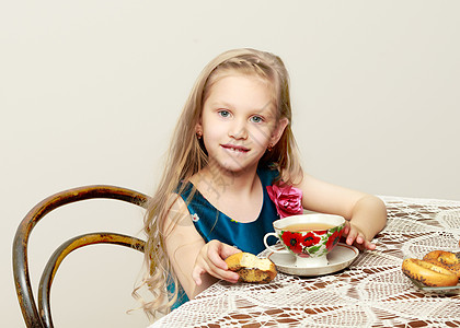 一个美丽的小女孩 长着金发的长头发坐在桌子上嘴唇微笑女性杯子公主冒充工作室幸福卷曲盘子图片