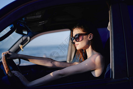 以时装旅行方式驾驶汽车的妇女头发微笑太阳镜车轮窗户乘客女性魅力司机镜子图片