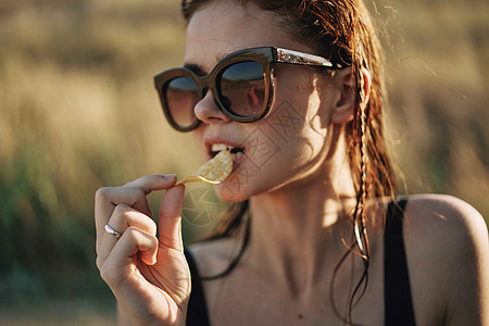 在自然阳光下吃薯片的太阳镜上小吃女性女孩帽子女士饮食成人垃圾营养微笑图片