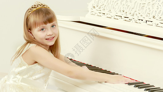 一个女孩在白色大钢琴旁边摆姿势旋律音乐卷曲童年女儿学校冒充孩子快乐公主图片