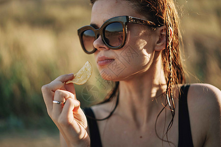 在自然阳光下吃薯片的太阳镜上帽子午餐垃圾食物营养成人女性青少年饮食筹码图片