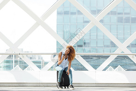 快乐的女人坐在站台上的手提箱上 看着手机图片