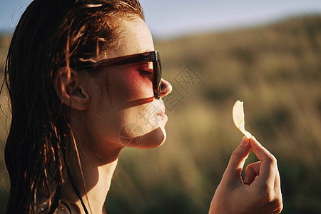 在自然阳光下吃薯片的太阳镜上女士食物青少年芯片女性垃圾帽子微笑成人小吃图片