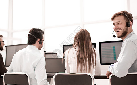 年轻的客户服务代理在办公桌前就座管理人员操作员顾客教育男人训练耳机推销职员工作图片