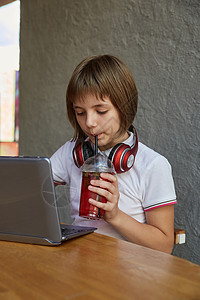 小女学生通过稻草喝柠檬水 在咖啡馆使用笔记本电脑图片