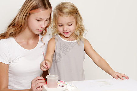 两个女孩在一张纸上涂油漆朋友们闲暇房子姐姐铅笔工作室快乐童年绘画刷子图片