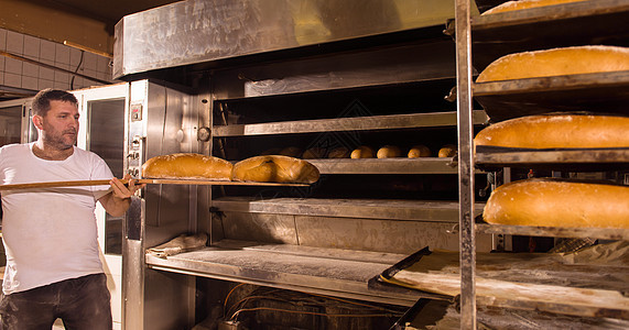 面包工人把新鲜烘烤面包拿出来推杆围裙男人工作服货架美食职场工厂食物手套图片