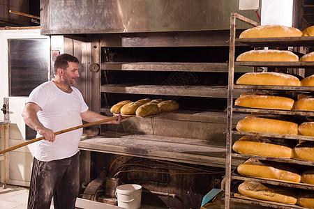 面包工人把新鲜烘烤面包拿出来食物推杆工作男人职业工厂货架工作服成人生产图片