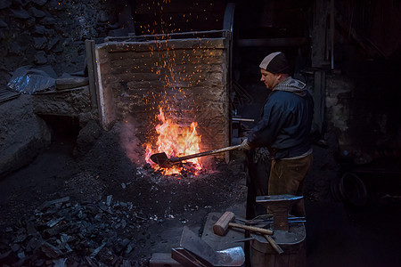 年轻的传统铁匠与开着的火一起工作火焰把手工人市场艺术火花工匠工具金属建造图片