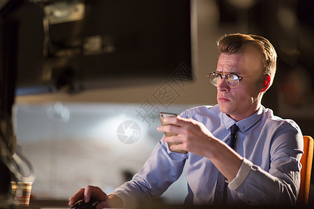 男子在暗办公室使用移动电话互联网阅读人士电脑办公室工作商业员工项目商务图片