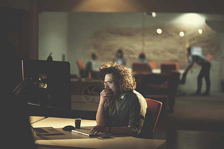 坐办公室的人在暗办公室从事计算机工作的男子互联网项目商务男性阅读监视器桌面屏幕程序员员工背景