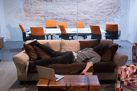 男人睡在有创意的办公室的沙发上男性人士工作商务笔记本成人说谎商业技术成功图片