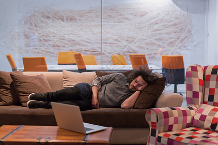 男人睡在有创意的办公室的沙发上职业桌子睡眠职场电脑笔记本员工技术商业人士图片