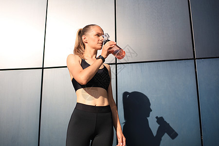 靠近一个年轻有吸引力的疲劳运动女运动员户外 从瓶子里喝水跑步液体茶点口渴活动女孩身体闲暇运动装慢跑者图片