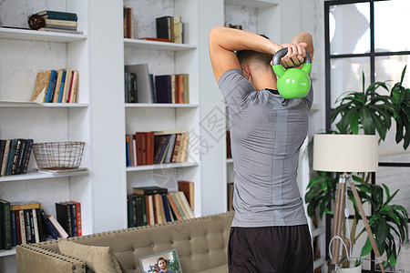 英俊的男子在家里用小叮当做运动 健康生活的概念地面训练男性房子运动装肌肉家庭健身房客厅闲暇图片