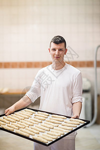 一个年轻面包师拿着白面粉的原始产品甜点店铺美食男性快乐生产面包职业工作托盘图片