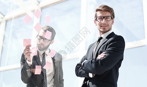 雇员读着贴在玻璃墙上的贴纸窗户公司职场同事办公室成功男人合作成人项目图片