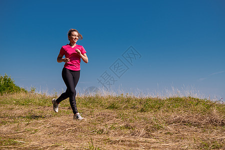 年轻女子在夏山阳光明媚的日子里慢跑活动运动员跑步训练日落女性耀斑草地太阳活力图片