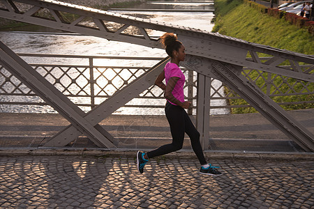 非洲裔美国妇女横跨大桥跑过人行道活力运动员赛跑者女孩训练城市运动慢跑公园图片