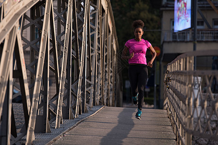 非洲裔美国妇女横跨大桥跑过人行道训练赛跑者慢跑者成人卷曲慢跑日出运动公园图片