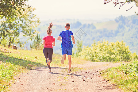 夫妻在乡村路上慢跑时享受健康的生活方式 在农村公路上游骑竞赛运动员活动太阳赛跑者男性女孩女士锻炼训练图片