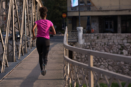 非洲裔美国妇女横跨大桥跑过公园人行道赛跑者运动跑步日落城市训练活力女孩图片
