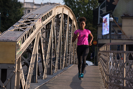 非洲裔美国妇女横跨大桥跑过成人女孩日落运动员活力运动慢跑者城市跑步人行道图片