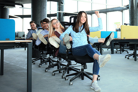 年轻快乐的商务人士穿着智能便衣 玩得开心 一边在办公室椅子上赛车 一边笑着笑休闲庆典竞赛工作商业运动友谊成人女性新生意图片