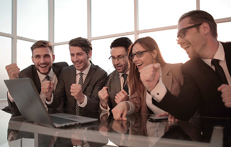 快乐的同事在办公桌上 举起手来优胜者工人合作欢呼笔记本幸福职场老板项目工作图片